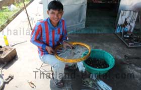 Ein Thai der gerade dabei ist in einer Werkstatt ein Vorderrad von einem Motorrad neue Speichen einzubauen.