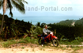 Ich, auf meinem in Thailand gemieteten Motorrad einer Enduro. Im Hintergrund die Bucht und das Meer, wenn man über die Palmen hinweg blickt.