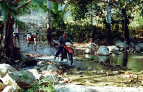 Mit einem gemieteten Motorrad kann man in Thailand, so wie bei uns auf dem Bild gezeigt fast überall biken. Auf dem Bild erkennt man wie wir gerade mit unseren Enduros durch einen kleinen Flusslauf fahren, mitten im Regenwald.