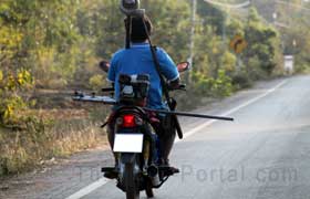 Ein Thailänder in Nordthailand auf einem Moped unterwegs der über der Schulter ein Jagdgewehr hängen hat.